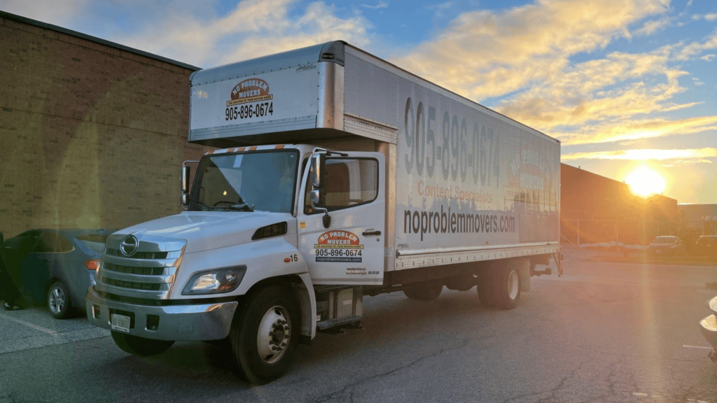 No Problem Movers branded moving truck parked outside a commercial building in Mississauga at sunset, ready to provide residential and commercial moving services.